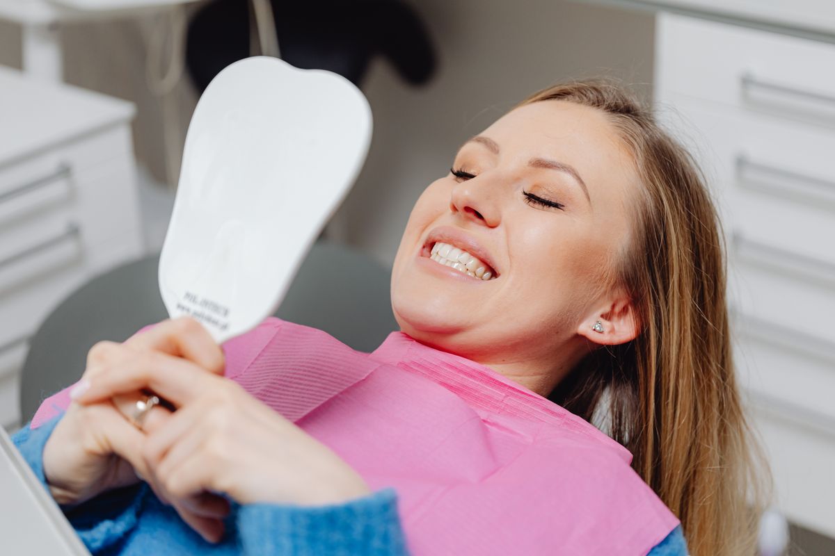 back tooth cavity filling Belapur, smiling patient checking a smile in a mirror at La Pearl Dental Boutique