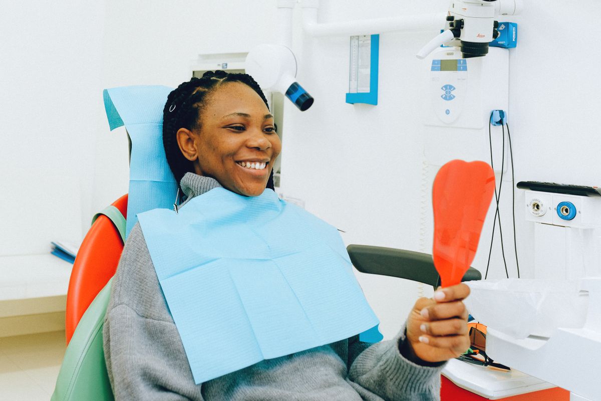 retainer after aligners Belapur, smiling woman holding a mirror at a dental check-up