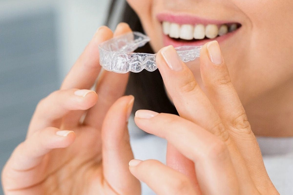Clear aligners CBD Belapur — a smiling woman holding a clear dental aligner at La Pearl Dental Boutique Navi Mumbai